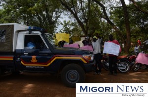 A police car passes demonstrators stand outside the Migori County Government gate  recently.